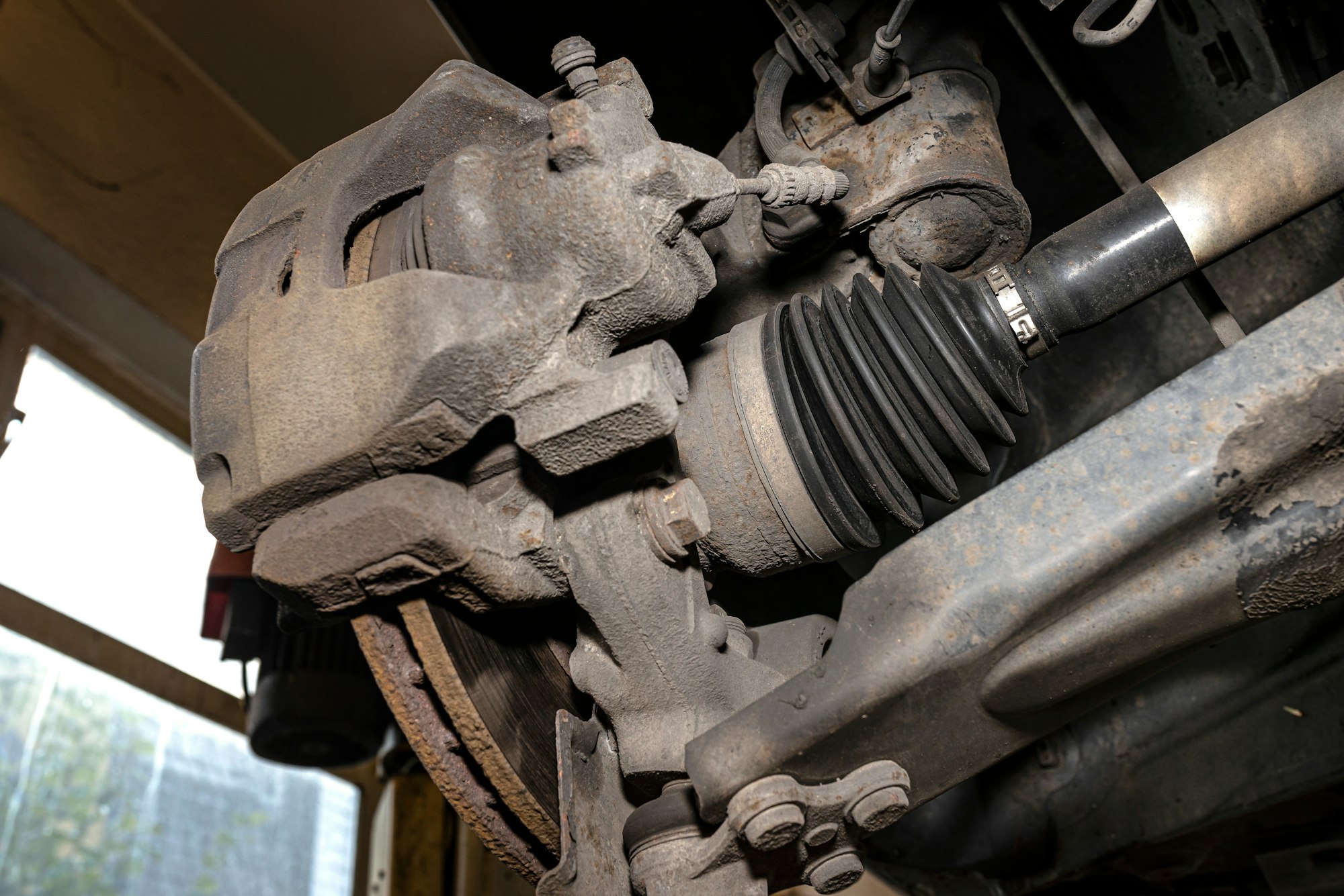 Drive shaft covered with rubber, visible disc and brake caliper, seen from the bottom of the car on
